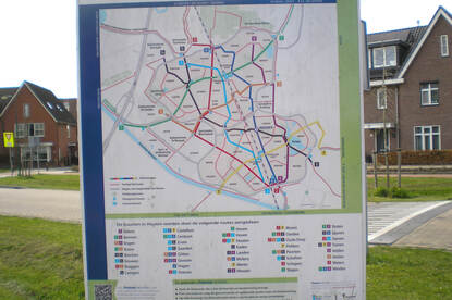 Een bord in een grasveld voor een woonwijk met daarop het fietsnetwerk van Houten.
